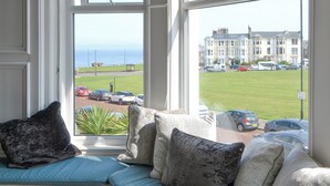 A room with a view of a grassy area and parked cars through a window. - Percy Park Apartment (TYNEMOUTH)