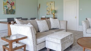 A living room with a sectional sofa, a glass coffee table, a patterned armchair, and a door. - Percy Park Apartment (TYNEMOUTH)