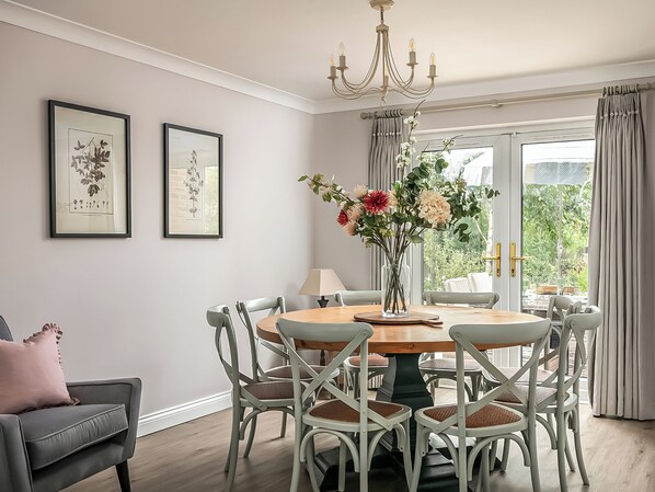 A dining room with a round table, white chairs, a chandelier, and framed botanical prints on the wall.