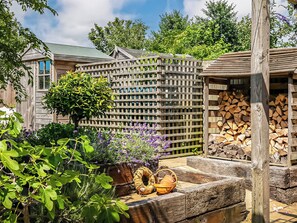 Ein Holzzaun, ein Holzstoß und ein Garten mit verschiedenen Pflanzen.