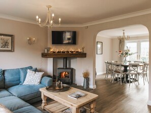 Ein Wohnzimmer mit Kamin, einer Couch, einem Couchtisch, einem Essbereich mit Stühlen und einer Chandelüster.