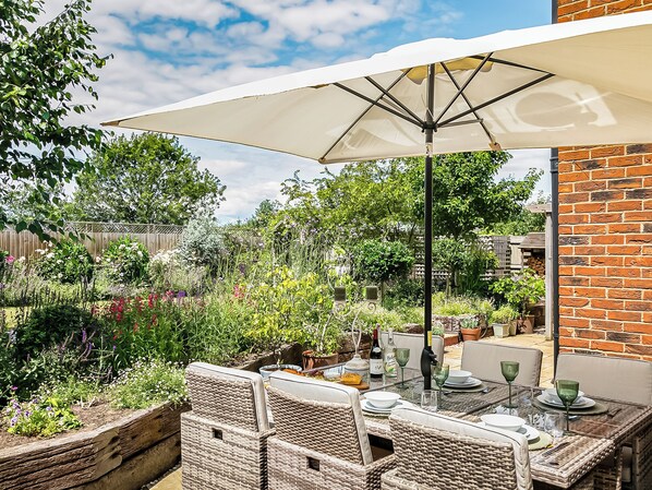 An outdoor patio with wicker furniture, a table set for dining, and a large umbrella providing shade.