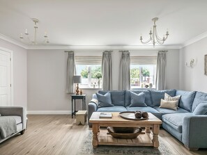 A living room with a blue sofa, a wooden coffee table, a chandelier, and a view of greenery outside.