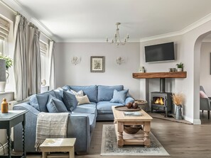 Ein Wohnzimmer mit einem blauen Sofa, einem Kamin, einem Fernseher und einer Chandelier.