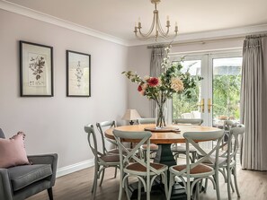 A dining room with a round table, white chairs, a chandelier, and framed botanical prints on the wall.