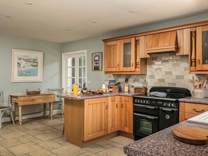 A kitchen with wooden cabinets, a granite countertop, a stove, and a dining area with a table and chairs.