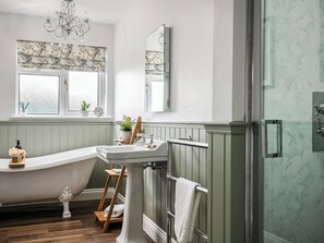 A bathroom with a freestanding bathtub, a sink, a mirror, and a shower area.