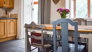 A kitchen with wooden cabinets, a dining table with two chairs, a window with curtains, and a heart-shaped decoration on the wall. - 2 bedroom accommodation in Dolwyddelan (Dolwyddelan)