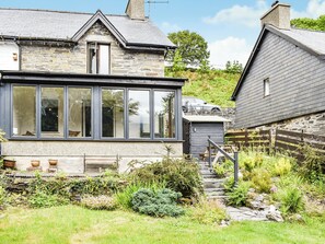 A stone house with a large glass window, a wooden deck, and a stone pathway leading to a door. - 2 bedroom accommodation in Dolwyddelan (Dolwyddelan)