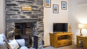 A cozy living room with a stone fireplace, a television on a wooden stand, and a lamp on a side table. - 2 bedroom accommodation in Dolwyddelan (Dolwyddelan)