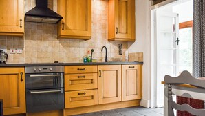 A kitchen with wooden cabinets, a black stove, and a tiled backsplash. - 2 bedroom accommodation in Dolwyddelan (Dolwyddelan)