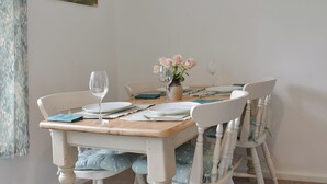 A dining table set with plates, a vase of flowers, and wine glasses, surrounded by white chairs with blue cushions. - 2 bedroom accommodation in Wool, near West Lulworth (Wool, near West Lulworth)