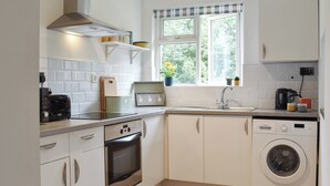 A compact kitchen with white cabinets, a built-in oven, a washing machine, and a window with a view of greenery. - 2 bedroom accommodation in Wool, near West Lulworth (Wool, near West Lulworth)