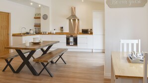 Une cuisine moderne avec des meubles blancs, une hotte en acier inoxydable, un four encastré et une table à manger en bois avec des bancs.