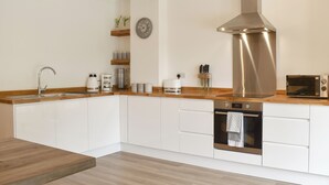 Une cuisine moderne avec des armoires blanches, une hotte de cuisinière en acier inoxydable, un four encastré et un four à micro-ondes.