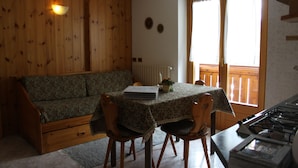 Et hyggeligt rum med trævæg, sofa, bord med stole, vindue med gardiner og en komfur.