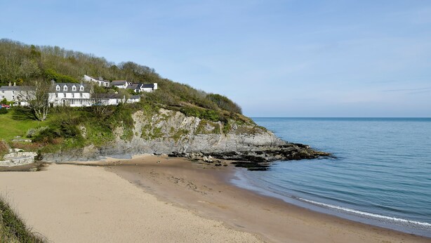 A coastal landscape with a sandy beach, a rocky cliff, and a row of white buildings on a hillside. - Cwmporthman Farm Cwtch-UK34700 (Blaenporth)