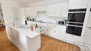 Une cuisine moderne avec des meubles blancs, un îlot central et deux fours.