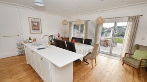 Une cuisine moderne dotée d’un îlot central, d’une table à manger et de chaises. On peut admirer la vue sur l’extérieur à travers la porte vitrée.