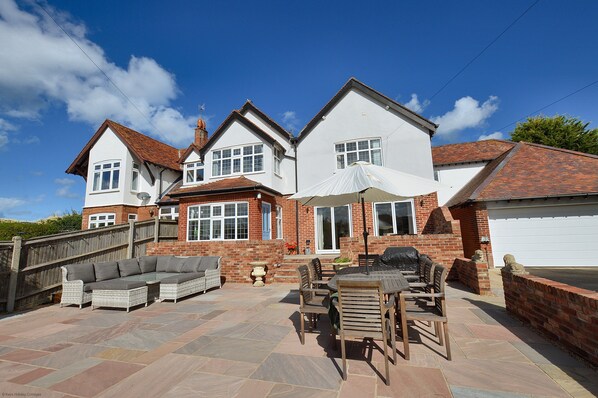 A two-story house with a patio area featuring a sofa set, dining table, and chairs.