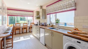 A modern kitchen with a dining area, large windows, and a washing machine.