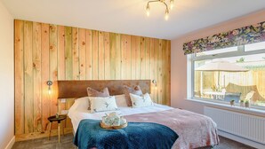 A bedroom with a wooden headboard, a bed with multiple pillows, a bedside table with a lamp, and a window with a view of an outdoor patio.