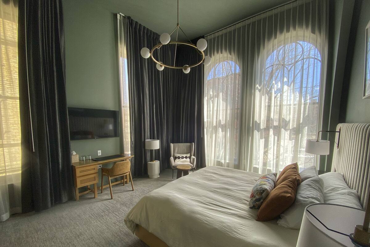 Une chambre d’hôtel avec un grand lit, un bureau avec un ordinateur, une chaise et un téléviseur fixé au mur.
