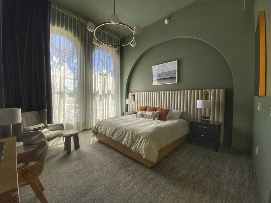 Camera d'albergo moderna con un letto grande, una scrivania e una sedia. Si vede una finestra con tende e una vista esterna.