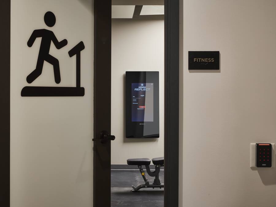 A fitness area with a sign, a digital kiosk, and exercise equipment.