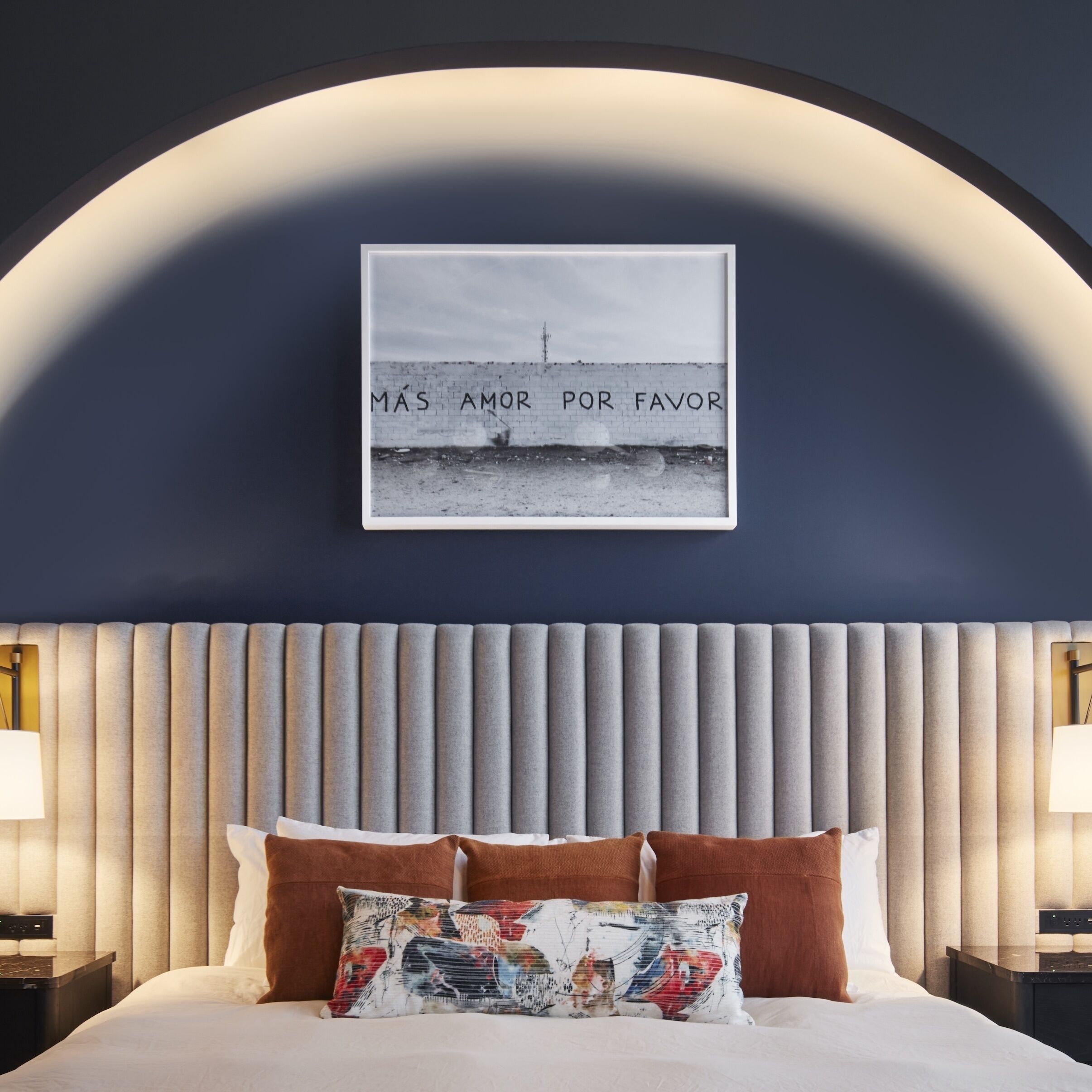 A bedroom with a bed, a headboard, a framed picture, and two bedside lamps.