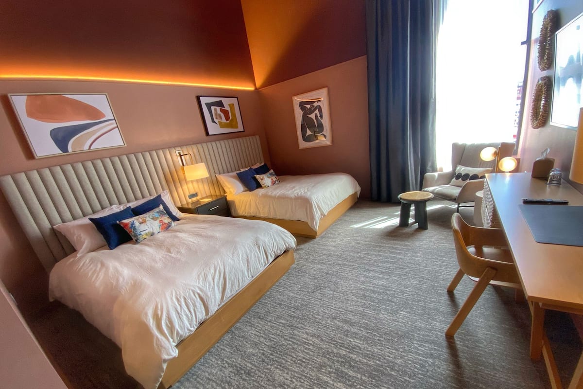 Une chambre d’hôtel avec deux lits, un bureau, une chaise et une petite table.