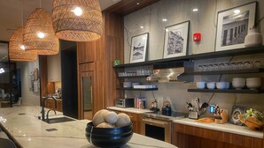 Una cocina moderna con encimera de mármol, un bol negro con bolas de madera, lámparas de mimbre colgantes y cuadros en la pared.