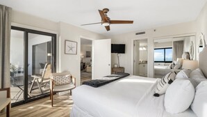 A spacious bedroom with a large bed, a ceiling fan, a TV, and a sliding glass door leading to a balcony. - Emerald Towers 902 (Destin)