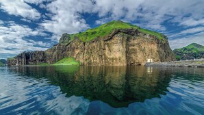 A large, rocky island with a grassy top and a small structure on the shore. - Pier Apartments (Vestmannaeyjar)