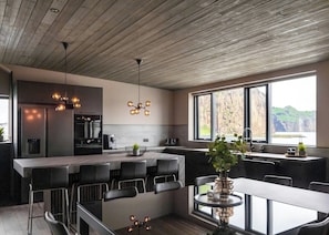 A modern kitchen with a central island, bar seating, and a large window offering a view of the outdoors. - Pier Apartments (Vestmannaeyjar)