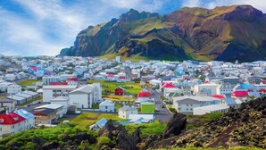 A coastal town with white buildings and red roofs, surrounded by mountains. - Pier Apartments (Vestmannaeyjar)