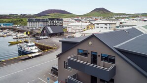 A coastal town with a marina, buildings, and a mountain in the background. - Pier Apartments (Vestmannaeyjar)
