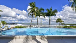 A swimming pool with a white fence, palm trees, and a view of the water. - Harbor Villa Club 305 (Longboat Key)