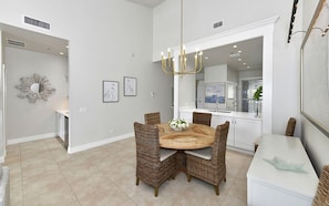 A dining area with a round wooden table, wicker chairs, and a chandelier.