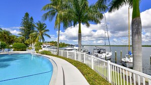 A swimming pool with a white deck, surrounded by palm trees and a marina with boats. - Harbor Villa Club 305 (Longboat Key)