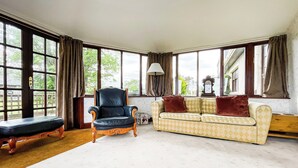 A spacious living room with large windows, a black leather armchair, a patterned sofa, and a wooden bench. - Fourpenny Studio - UK34745 (Skelbo, near Dornoch)