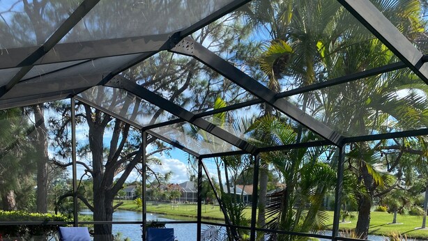 Uma área de piscina com um espaço coberto para sentar, piscina com água azul cristalina, e vista para um lago e árvores.