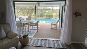 Sala de estar com sofá, mesa de centro e vista para a área da piscina externa.