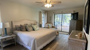 Um quarto com cama, mesas de cabeceira, cômoda, televisão e ventilador de teto.