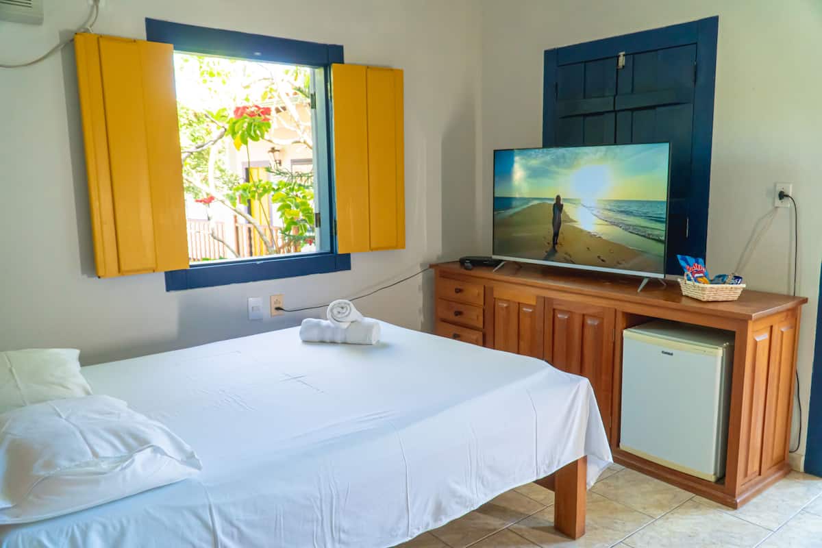 Quarto com cama, televisão em um armário de madeira e janela com persianas amarelas.
