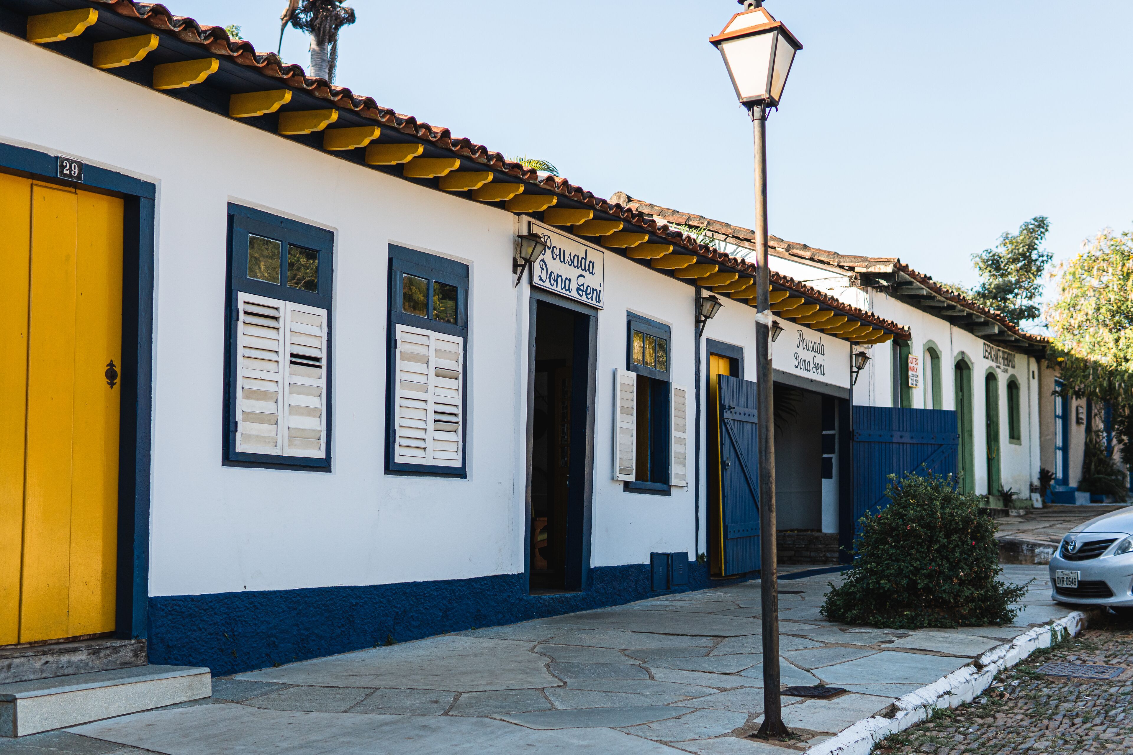 Una hilera de edificios con paredes blancas y detalles azules, puertas amarillas y una calle empedrada.