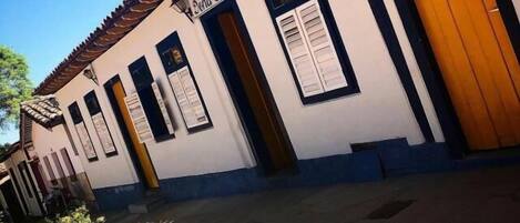 A building with a tiled roof, white walls, and wooden doors. There is a sign on the wall that reads "Pousada Dona Geni."