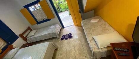 A compact hotel room with two single beds, a small desk with a computer, and a ceiling fan.