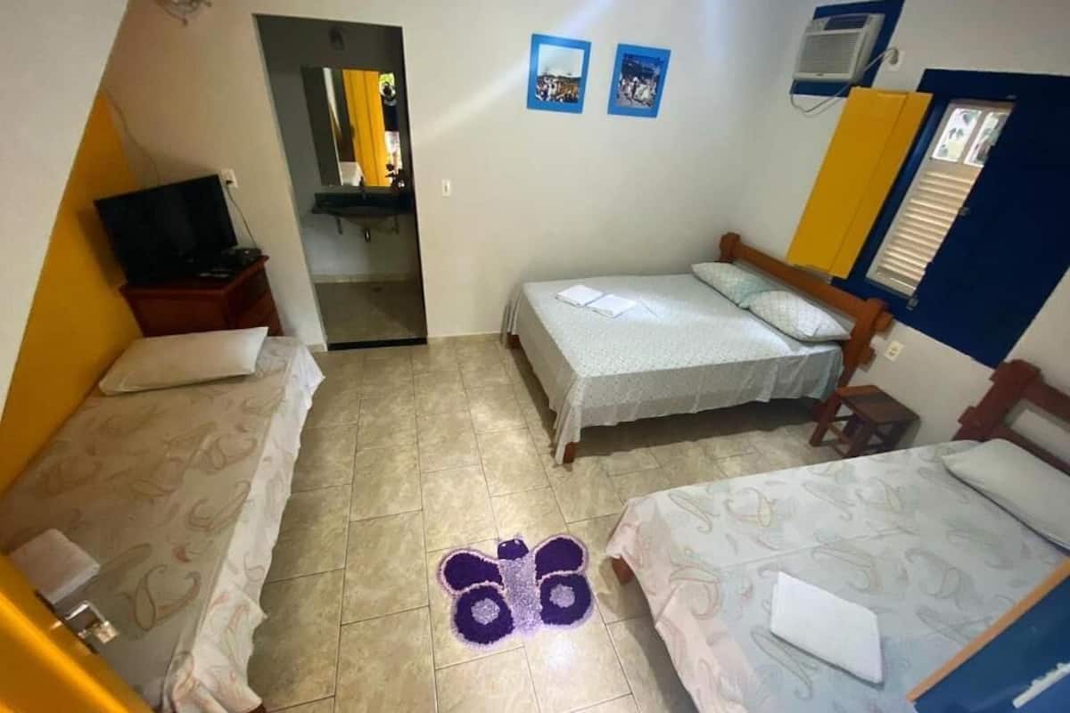 Quarto pequeno e compacto com duas camas de solteiro, televisão e banheiro visível por uma porta aberta.