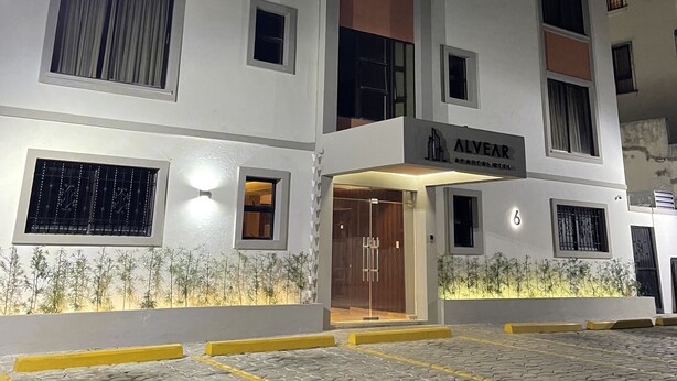 A multi-story hotel with a modern facade, a visible entrance with a glass door, and a sign indicating the name 'ALVEAR'. - Apartahotel Alvear (Santo Domingo)